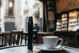 A sleek, minimalist vape resting on a table in a quaint European café, next to a cup of coffee.