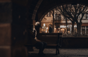 A person discreetly using a small, simple vape while sitting on a park bench in a foreign city.